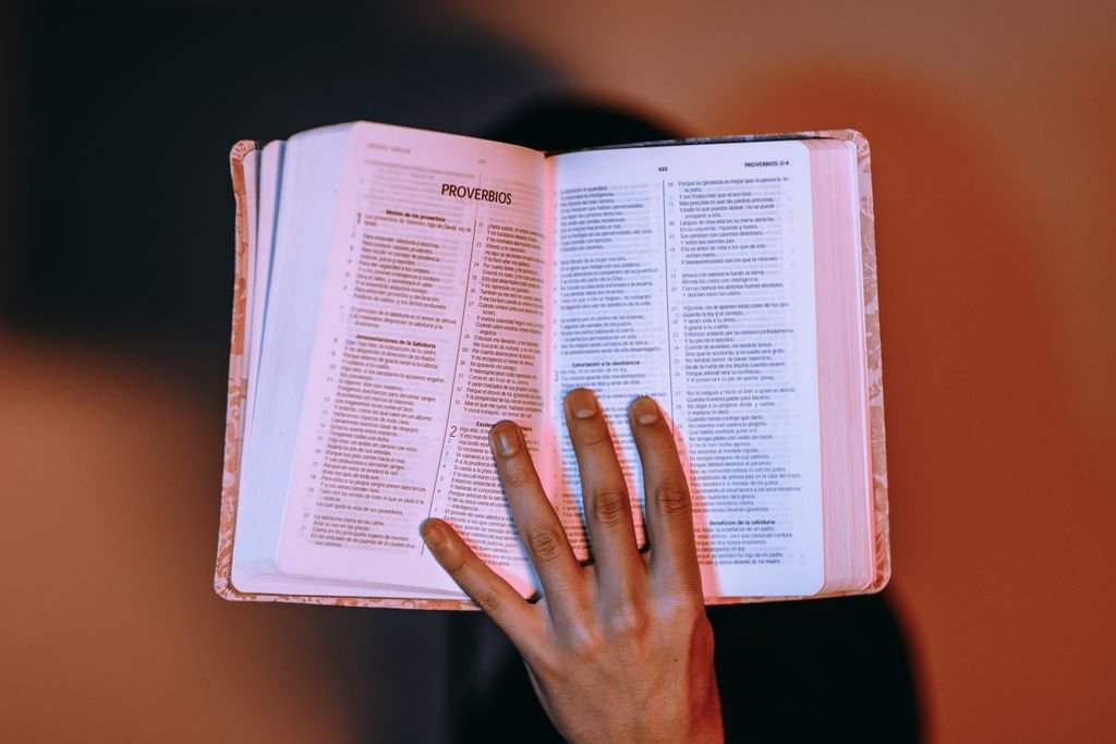 Foto de Luis Quintero A close-up of a hand holding an open Bible, displaying Proverbs under warm lighting.